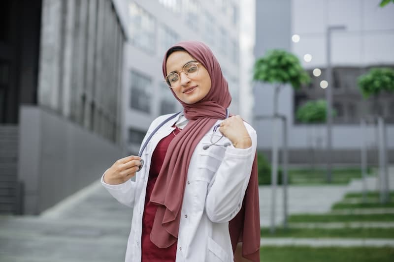 Muslim nurse wearing hijab and glasses with stethoscope outside modern clinic