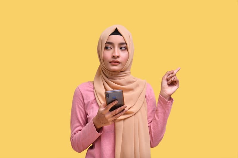 Wanita berhijab memegang telefon dan membandingkan alat foto profesional AI